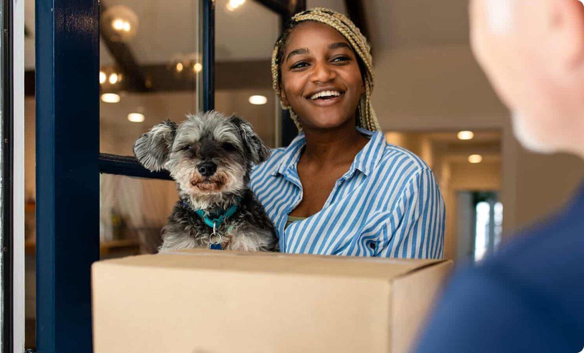 A woman holds her dog and receives a package at her house.